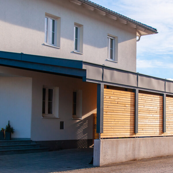 Moderner Carport aus Holz mit integrierter Holzverkleidung an einem weißen Wohnhaus