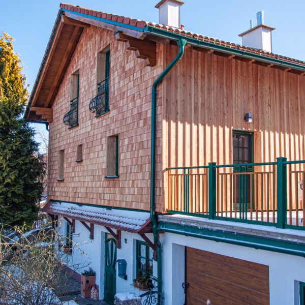 Wohnhaus mit vertikaler und Schindel-Holzfassade, großem Balkon und Garage, fotografiert bei Winterwetter