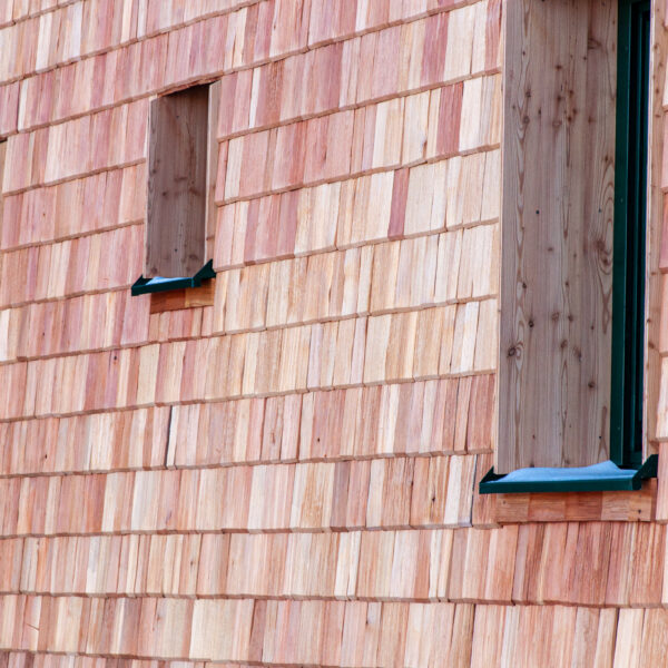 Nahaufnahme einer Holzschindelfassade mit schmalen, hochformatigen Fenstern