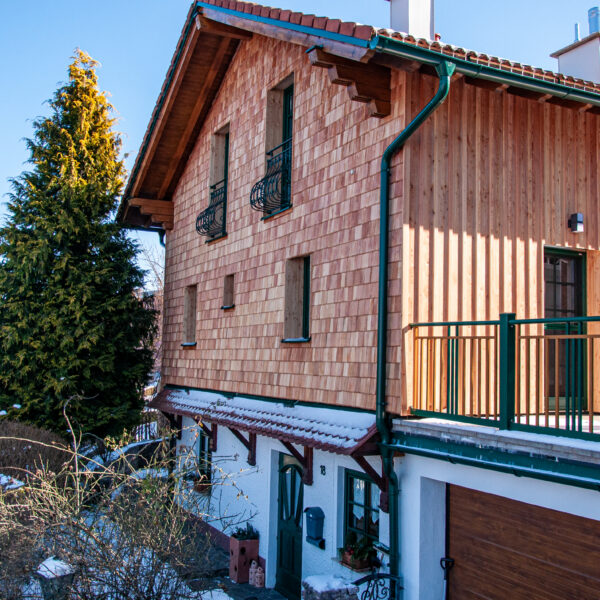 Schrägansicht eines Wohnhauses mit Holzfassade, Garten, Straße und winterlicher Umgebung