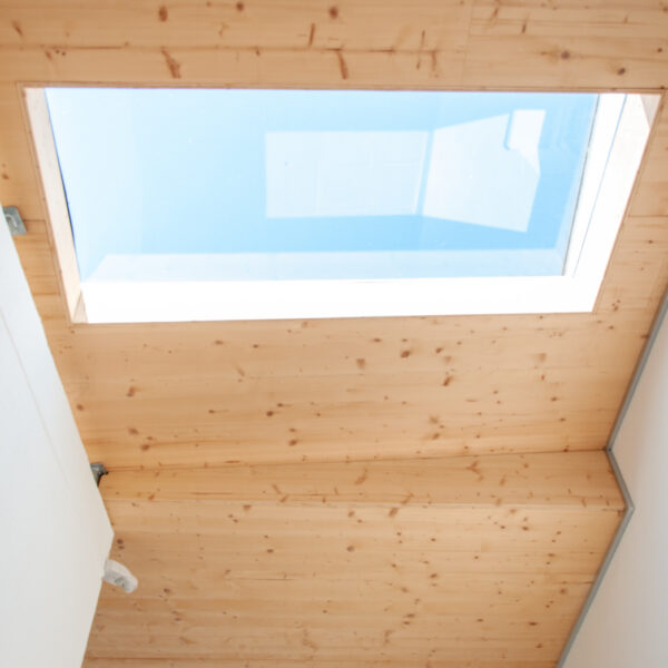 Blick durch ein Oberlicht im Holzplafond eines überdachten Durchgangs.