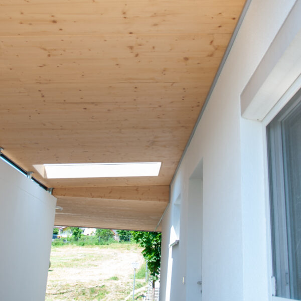 Überdachter Hausdurchgang mit Holzdecke, Oberlicht und weißen Wänden.